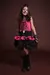 Menina sorridente vestindo fantasia de Caveira Punk, com vestido rosa e saia preta de camadas, botas pretas e acessórios temáticos.