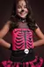 Menina sorrindo vestida de Caveira Punk, com maquiagem temática e um vestido rosa com estampa de ossos.