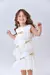 Menina sorrindo usando um vestido branco com laços dourados e camadas de tule.