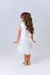 Menina de costas usando um vestido branco com camadas e laços dourados.