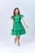 Menina sorridente usando um vestido de festa verde com tule, posando em um fundo neutro.