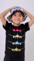 Criança sorridente usando uma camiseta preta com estampa de aviões coloridos, segurando um chapéu com padrão preto e branco.