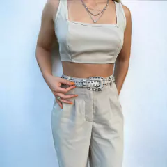 mulher usando cinto off white de couro off white estilo western, com aplicações de tachas metálicas em toda a extensão e fivela decorada