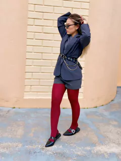mulher usando look com meia vermelha, blazer cinza, sapatilha preta e cinto feminino preto em material sintético, com ilhós metálicos e correntes prateadas removíveis como detalhe decorativo