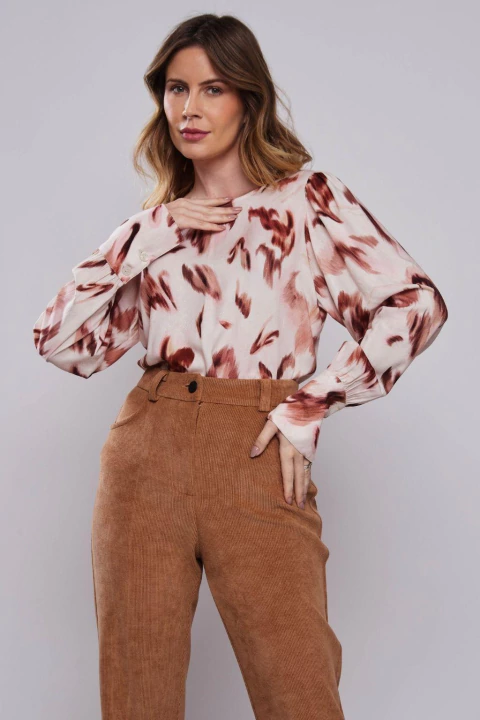 Mulher vestindo blusa de manga longa com estampa de onça aquarelada em tons terrosos, combinada com calça bege de alfaiataria. Peça elegante ideal para look office e ocasiões sofisticadas.