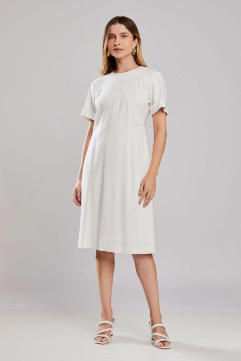 Mulher vestindo vestido midi risca de giz Louvre off white, com mangas curtas e sandálias brancas, ideal para o verão.