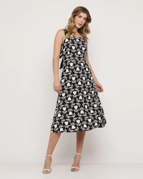 Modelo vestindo vestido longo evasê preto com estampa floral branca, alças finas e saia rodada, ideal para ocasiões casuais ou eventos.