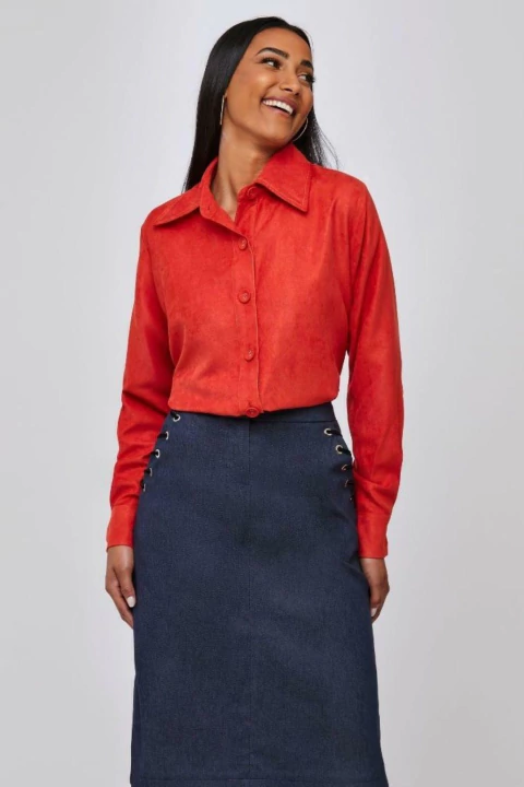 Mulher vestindo camisa fraldada de alfaiataria na cor laranja com saia azul-marinho.