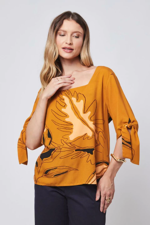Mulher vestindo blusa manga comprida com estampa floral em tons de amarelo mostarda