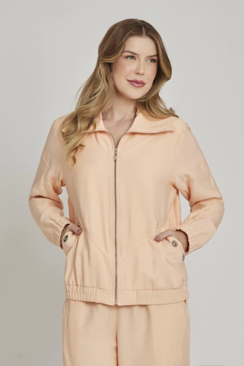 Mulher vestindo jaqueta feminina salmão com ilhós e zíper frontal, ideal para looks casuais e esportivos.