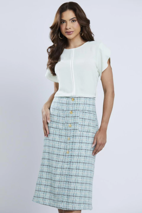 Mulher vestindo blusa bicolor Orvalho de manga curta em tom claro, combinada com saia midi xadrez, visual casual e elegante.
