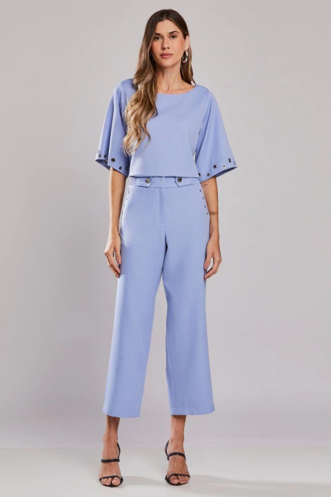 Mulher vestindo calça reta ampla azul com ilhós, modelo de alfaiataria elegante para look office, verão 25/26.