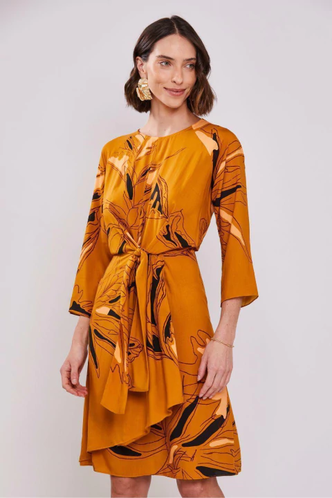 Mulher vestindo um vestido evasê com mangas 7/8 em estampa floral abstrata, cor laranja.