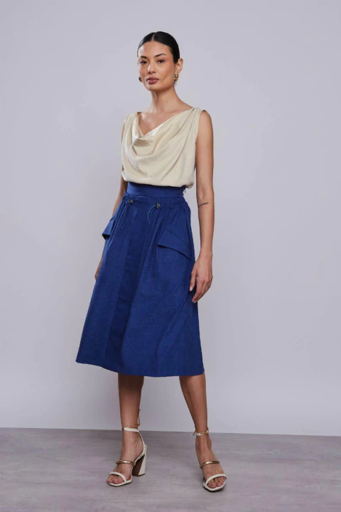 Modelo vestindo saia midi azul escuro, combinada com blusa clara e sandálias de salto.