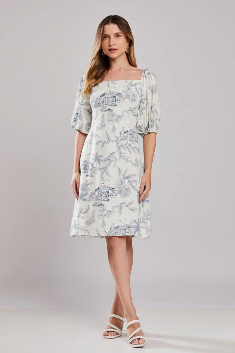 Mulher vestindo o Vestido Mangas Bufantes Porto, modelo midi com estampa delicada em azul, mangas bufantes e decote quadrado, ideal para o verão.