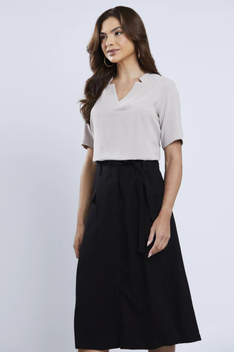 Mulher vestindo blusa fluida com decote V na cor fendi, combinada com saia preta, em fundo neutro.