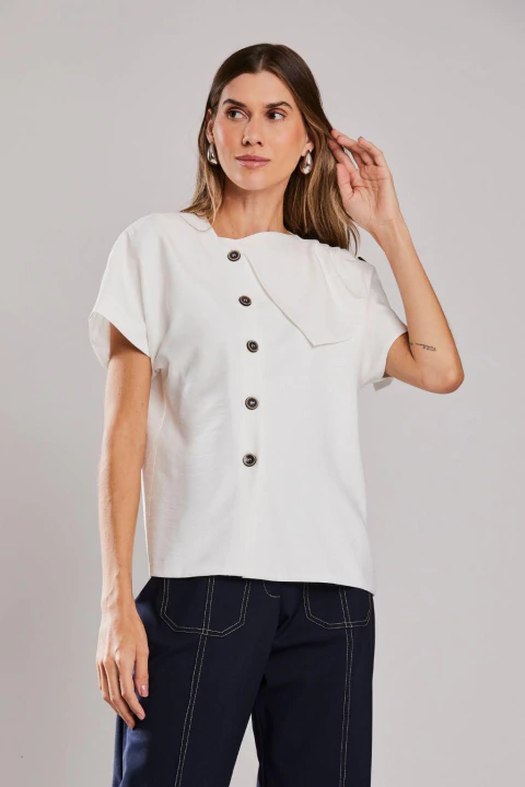 Mulher vestindo blusa assimétrica de alfaiataria off white, com botões frontais, ideal para looks elegantes de verão ou office look.