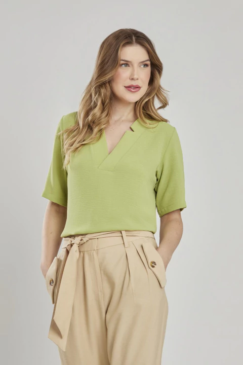 Mulher vestindo blusa fluida verde folha com decote em V e manga curta, combinada com calça bege de cintura alta e cinto.