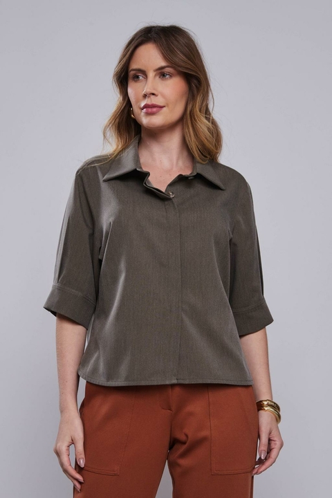 Mulher vestindo camisa manga curta alfaiataria Pinho em tom escuro, combinada com calça marrom.