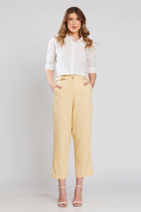 Mulher vestindo calça reta Sintra na cor amarelo claro, combinada com camisa branca e sandálias de salto, ideal para looks elegantes de verão ou office look.