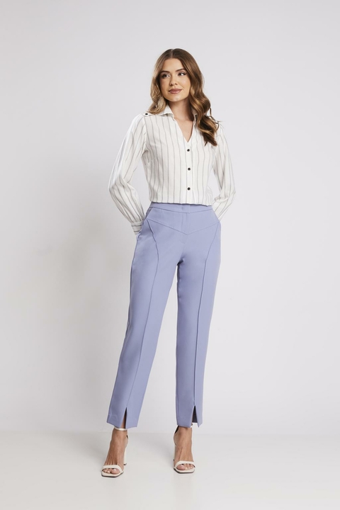 Mulher vestindo calça fenda frontal azul bebê e camisa listrada, em um look de alfaiataria feminina.