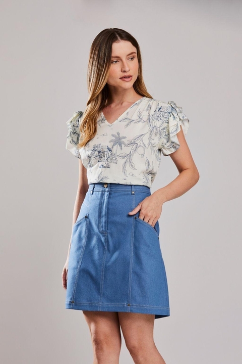Mulher vestindo blusa Babados Porto Unica com estampa floral e babados nos ombros, combinada com saia jeans azul. Moda casual feminina de verão.