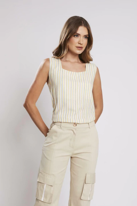 Mulher vestindo regata Coração Unica listrada em tons claros, combinada com calça bege, em fundo branco.