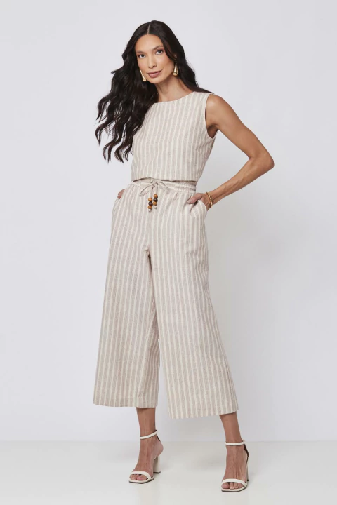 Mulher vestindo uma calça pantacourt listrada em tom claro, combinada com blusa sem mangas e sandálias de salto alto.