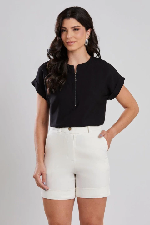 Mulher vestindo blusa básica preta com zíper e mangas curtas, combinada com shorts branco, ideal para looks casuais e de verão.