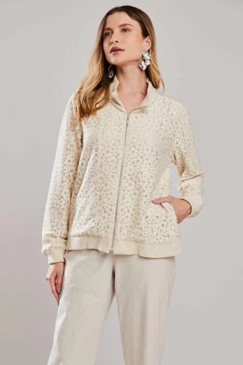 Mulher vestindo jaqueta esportiva em renda na cor aveia, com zíper frontal e bolsos laterais, ideal para o verão.