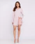 Mulher vestindo camisa longa listrada única e shorts rosa claro, em pose casual.