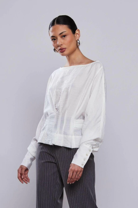 Mulher vestindo blusa off white com amarração, mangas longas e botões nos punhos, ideal para o inverno.