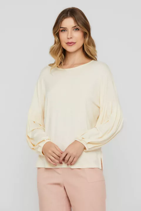 Modelo vestindo blusa Rubinella com mangas bufantes e decote redondo, na cor cru.