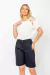 Modelo vestindo Bermuda Sarja Basic preta com blusa branca de alças entrelaçadas.