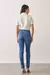 Modelo vestindo calça jeans skinny azul Andreza vista de costas, combinando com blusa branca e sandálias de salto alto.