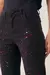 Calça jeans reta preta com respingos coloridos, vista frontal do detalhe na altura da cintura e pernas.