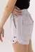 Short curto de cintura alta com ilhós Cristina na cor cinza mescla, detalhe lateral com bolsos e acabamento em ilhós, sendo usado por modelo.