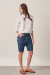 Modelo vestindo a Bermuda Jeans Feminina Lilith com camisa branca oversized e mocassins marrons