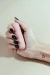 Uma mão segurando um vibrador recarregável rosa da marca MY ONE, com unhas pintadas de preto.