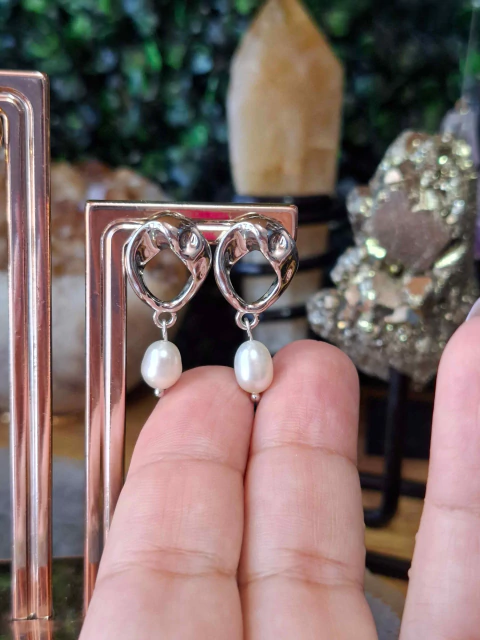 Brinco prateado com design orgânico e pérola de água doce pendurada, exibido sobre dedos femininos