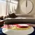 Tapete redondo moderno com design geométrico colorido, em um ambiente de sala com sofá curvo e parede decorativa.