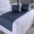 Peseira de cama em tom azul escuro com almofadas cinzas sobre uma cama branca.
