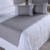 Peseira de cama cinza em um colchão branco, acompanhada por almofadas retangulares.