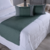 Peseira de cama na cor verde com almofadas cheias, sobre colcha branca em ambiente moderno.