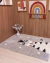 Tapete infantil de algodão com estampa de zebra em um ambiente acolhedor, decorado com quadros e um vaso de algodão.