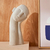 Escultura decorativa de poliresina com formato de rosto, medindo 13x38 cm, posicionada sobre uma superfície clara.