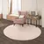 Tapete redondo off-white na sala, com uma cadeira rosa e uma mesa lateral.