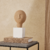 Escultura abstrata de poliresina bege com base branca, sobre uma mesa decorativa.