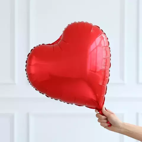 Globo metálico en forma de corazón color rojo de 14 pulgadas sostenido por una mano.