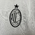 Camisa branca do AC Milan com detalhes em vermelho e preto, exibindo logo da equipe e patrocinadores.
